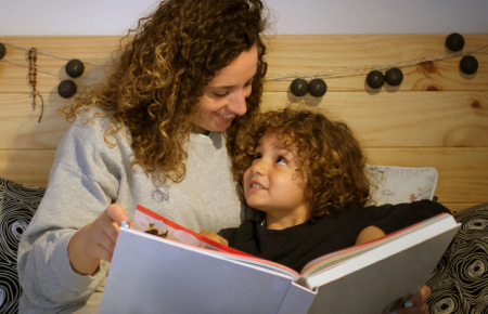 Child looks up lovingly at parent who reads picture book to them at bedtime