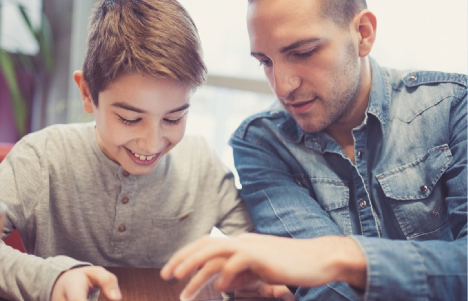 A person sitting next to a smiling teenager holding and looking at an ipad screen. 