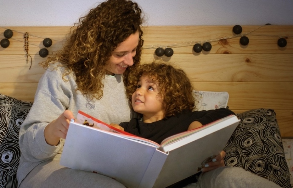 Child looks up lovingly at parent who reads picture book to them at bedtime