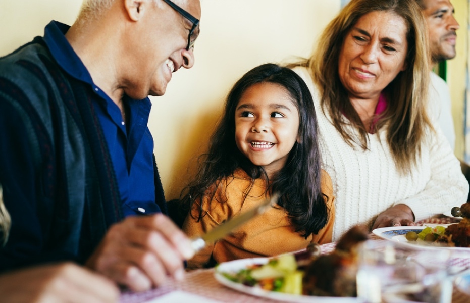 A smiling child sitting between two smiling adults at a dinner table.