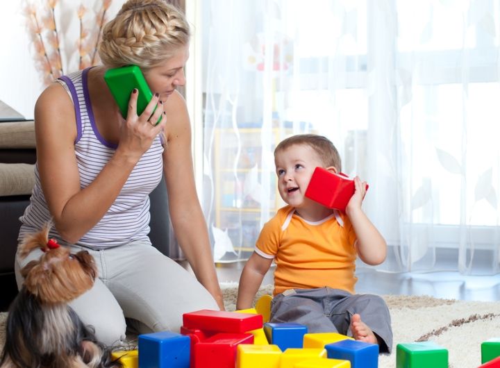 mother playing pretend telephone with little boy using building blocks
