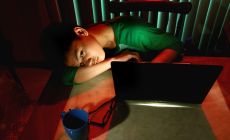 teenage boy lying slumped in front of computer at night
