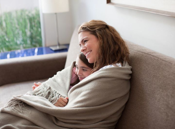 mother and daughter snuggle under blanket while watching TV